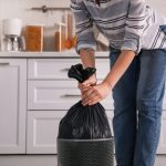 Woman taking garbage bag out of bin at home, closeup