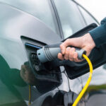 Man plugging in charger into an electric car at charge station